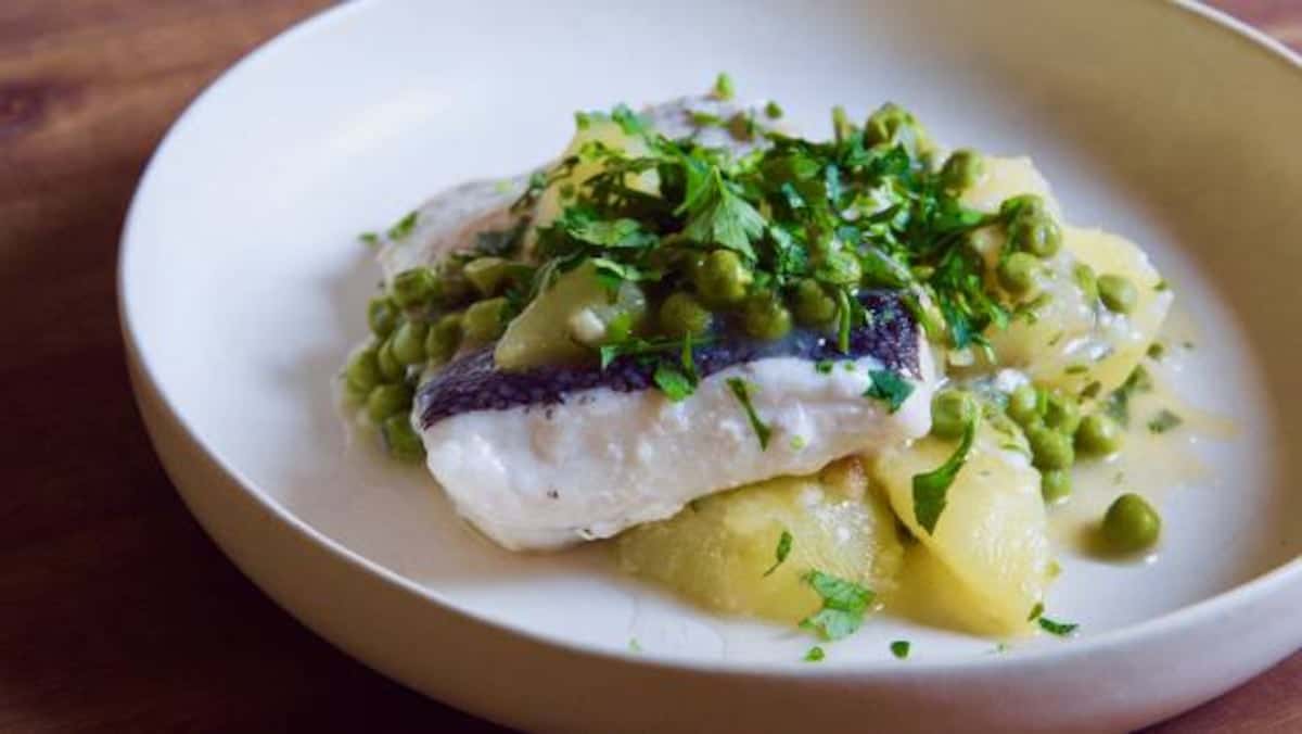 Cazuela tradicional de barro con merluza en salsa verde brillante, decorada con gambas y perejil picado